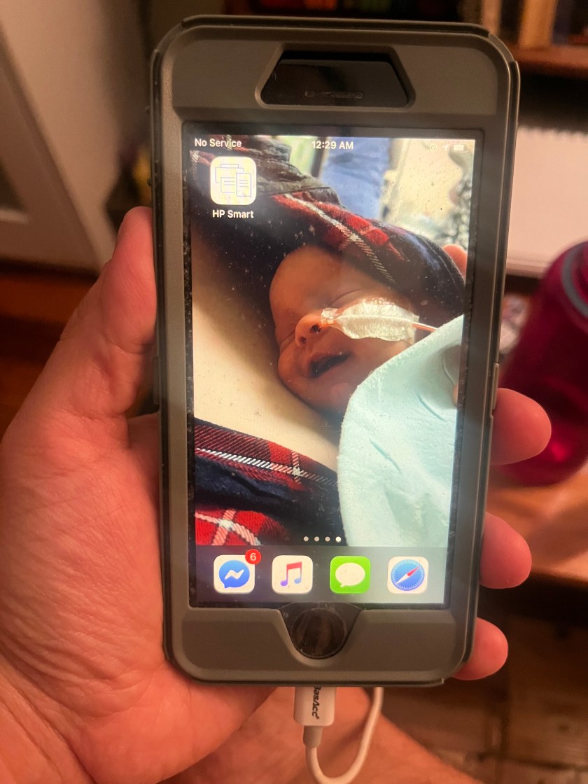 A picture of a hand holding a smartphone with an image of a baby tucked onto someone's chest